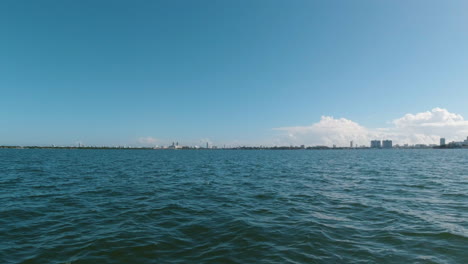 Blick-Auf-Den-Wasserstand-Eines-Kleinen-Wasserfahrzeugs,-Das-Sich-Einer-Stadt-Am-Horizont-Mit-Blauem-Wasser-Und-Sonnigem-Blauem-Himmel-Nähert