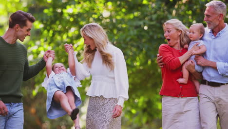 portrait of multi-generation family enjoying walk in countryside together swinging granddaughter