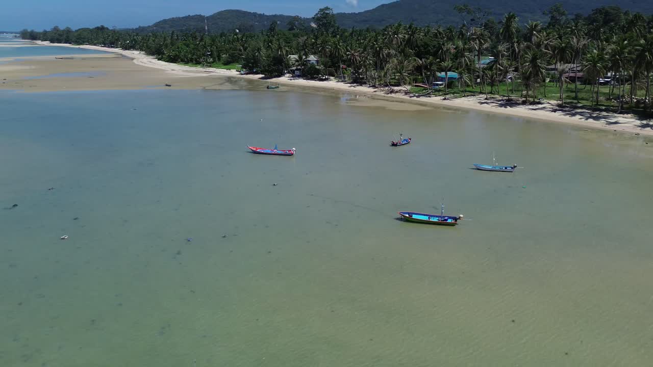Stunning drone footage captures traditional Thai fishing boats resting on the clear, shallow waters off Koh Phangan island in Thailand. A serene tropical landscape island scenery