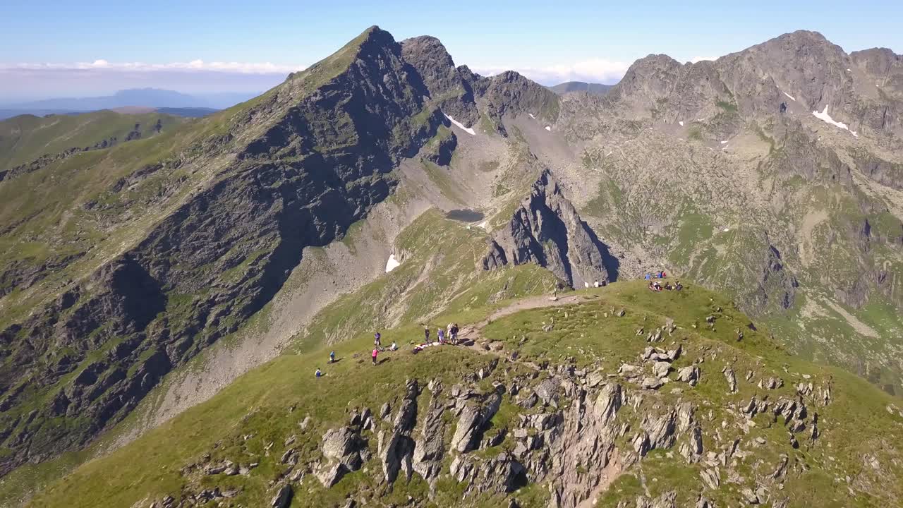 amplia vista aérea de escaladores en la cumbre de la montaña con hierba verde y cielo azul brillante