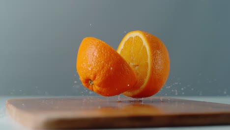 Zwei-Orangenstücke-Fallen-Auf-Ein-Schneidebrett
