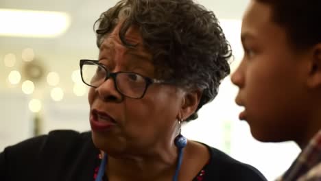 a senior woman passionately speaks to a young boy at a community gathering, sharing insights and fostering connection. their interaction reflects warmth and curiosity amid a lively atmosphere.