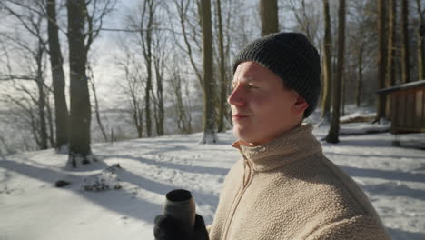 sunlit winter moment as a person sips from a thermos, enjoying a hot beverage in a snowy forest