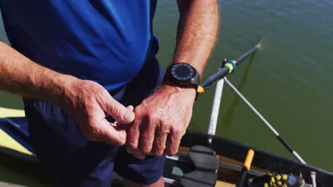 Senior-caucasian-man-standing-by-a-river-checking-smartwatch