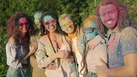 portrait of happy people covered with powder paint hugging and smiling standing outdoors