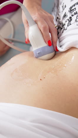 making ultrasound of baby in clinic office. pregnant woman laying on bed during ultrasound. doctor gynecologist performing screening belly of pregnant woman. top view. vertical video