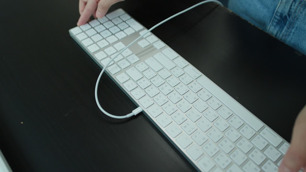Individual unboxes, connects, and arranges a wired keyboard on a dark desk under soft lighting