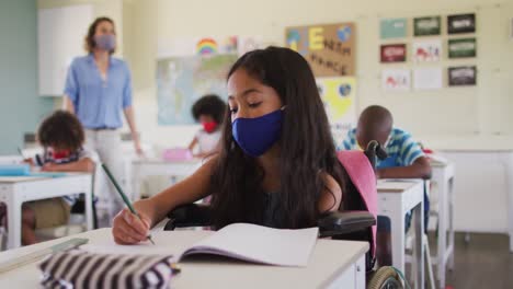 Deshabilitar-A-Una-Chica-Que-Usa-Mascarilla-Escribiendo-Mientras-Está-Sentada-En-Silla-De-Ruedas-En-Clase