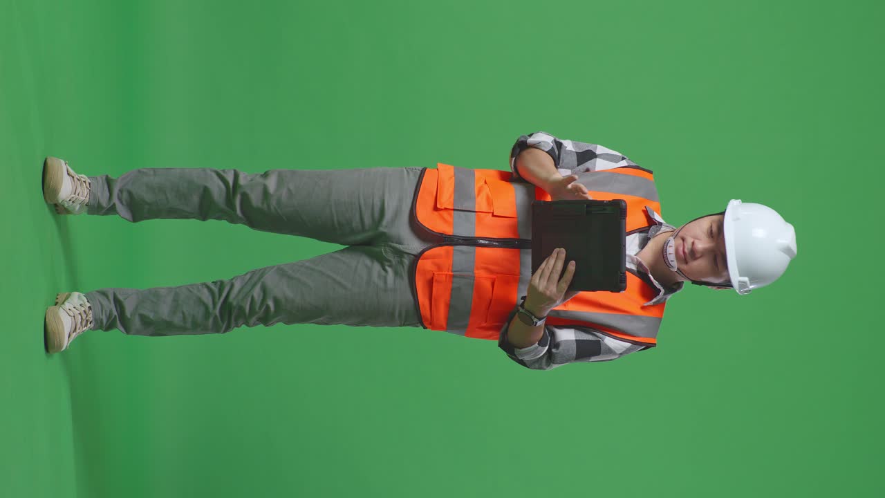 Full Body Of Asian Male Engineer With Safety Helmet Working On A Tablet While Standing In The Green Screen Background Studio