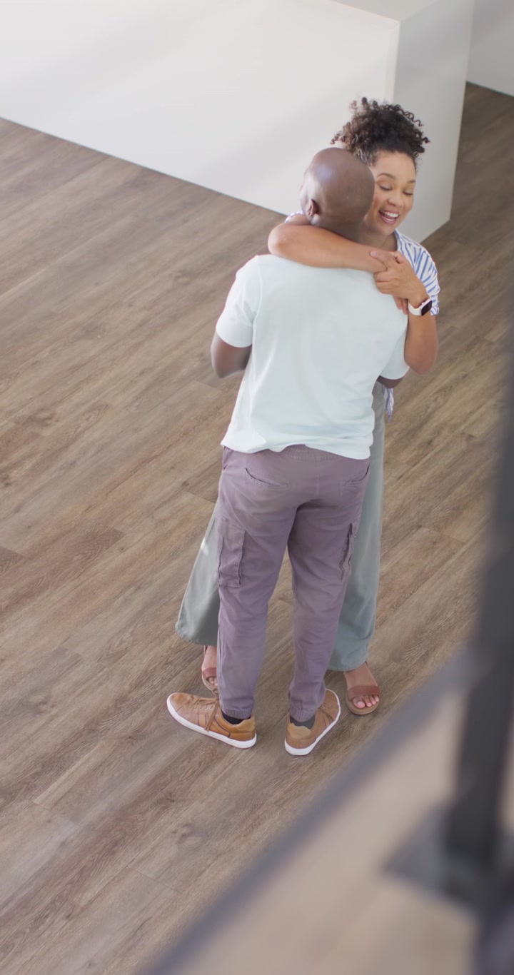 Vertical video: Couple embracing, swaying and stepping in empty room after moving in with box
