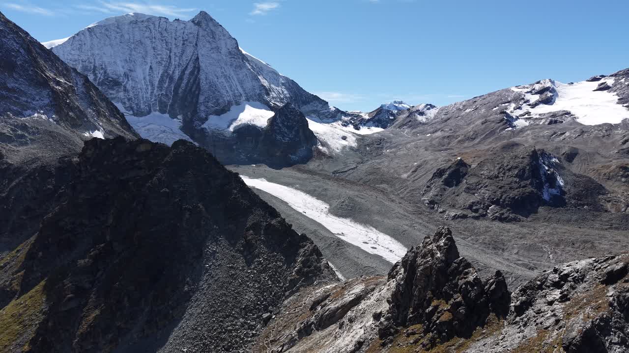 Sorvolo aereo sopra le scogliere accanto al Ghiacciaio di Cheilon, vicino ad Arolla, Svizzera, con una vista su un sentiero escursionistico che porta alla cresta del Pas de Chèvre e a cime come il Mont Blanc de Cheilon.