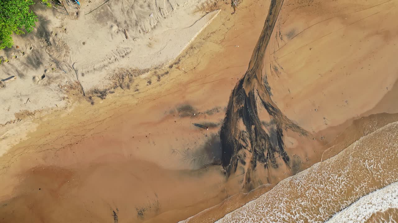 Top‑view spinning aerial highlighting the striking black sand patterns along the shoreline, with waves rolling in and lush tropical scenery at Quinawan Beach in Mariveles, Bataan, Philippines