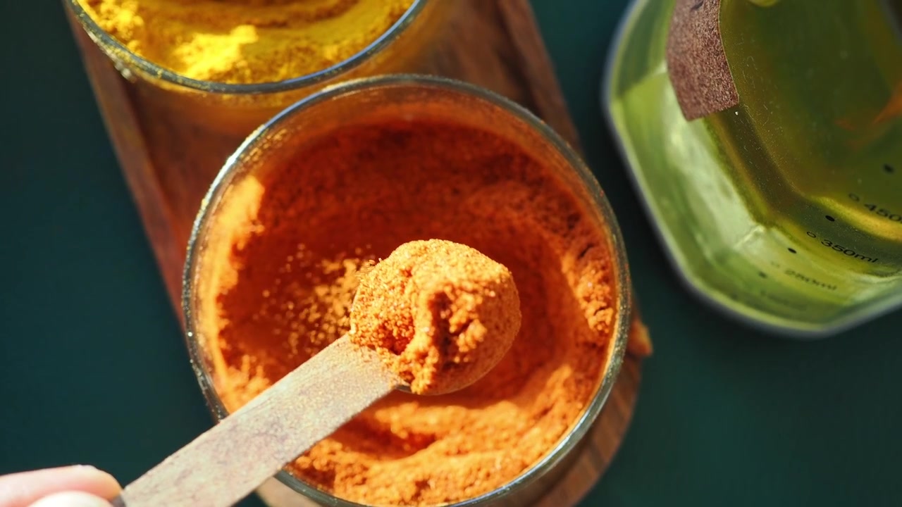 Hand Scooping Red Chili Powder with a Wooden Spoon