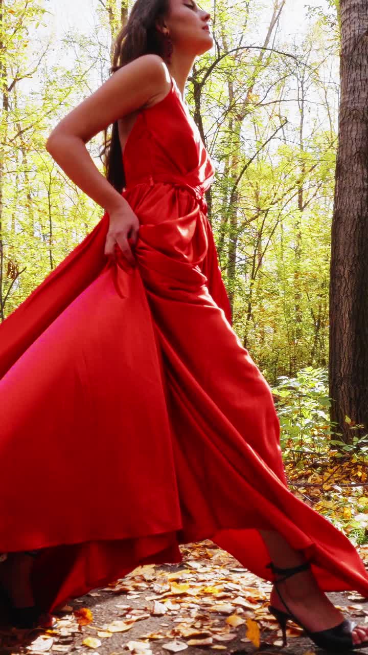 A Graceful Woman in an Elegant Red Dress Strolls Through a Sunlit Forest, Capturing the Essence of Autumn's Beauty and Fashion in Nature's Embrace