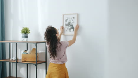 woman hanging picture on wall