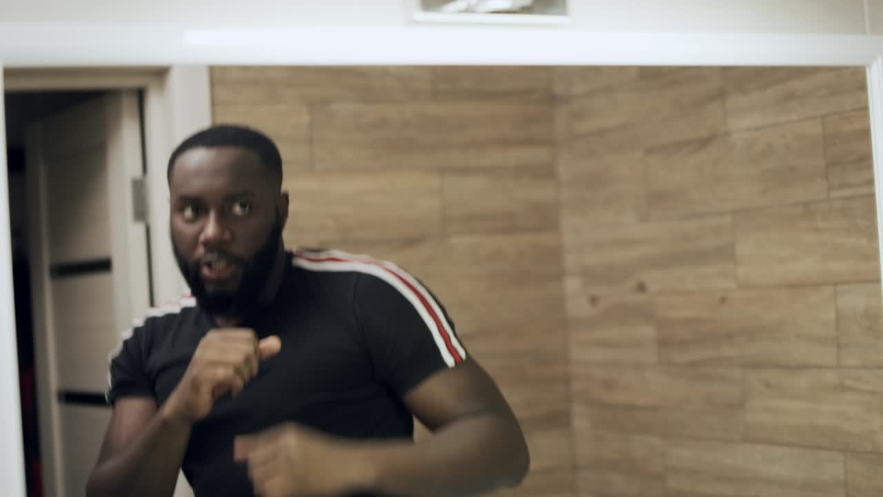 Aggressive black man boxing in front of mirror at bathroom.