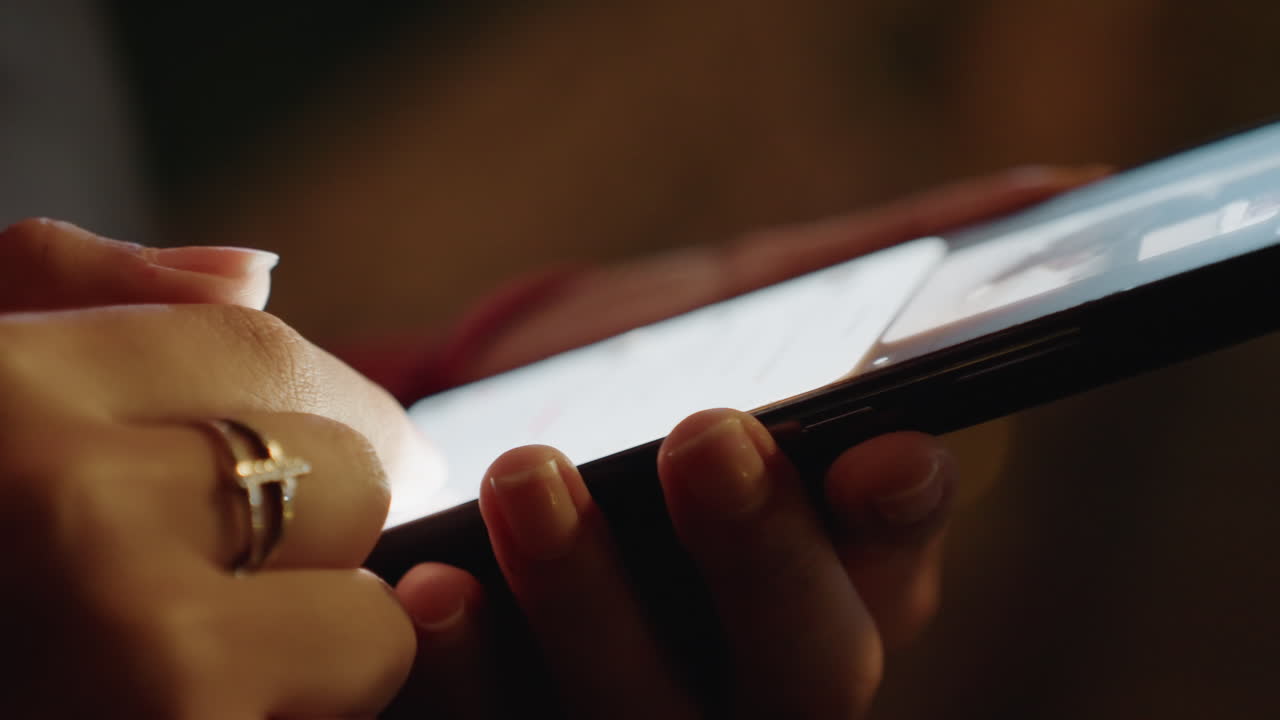Closeup female hands tapping smartphone screen in dim warm light, gold ring catching bokeh highlights, slow thumb scrolling through social feed, intimate latenight mood, soft shadows, cinematic