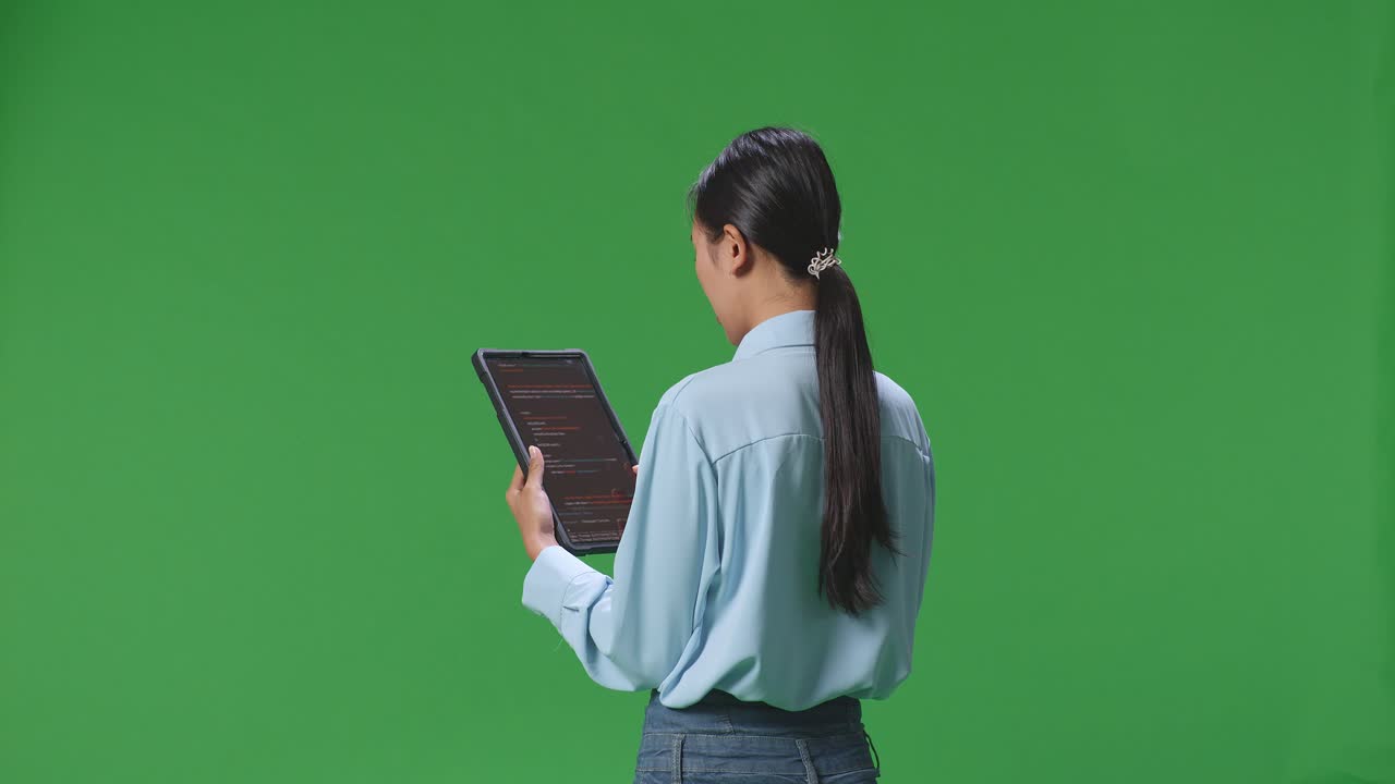 스튜디오에서 녹색 화면 배경에 태블릿을 사용하는 아시아 사업가 여성의 뒷면, 태블릿 디스플레이 코드를 보여줍니다.
