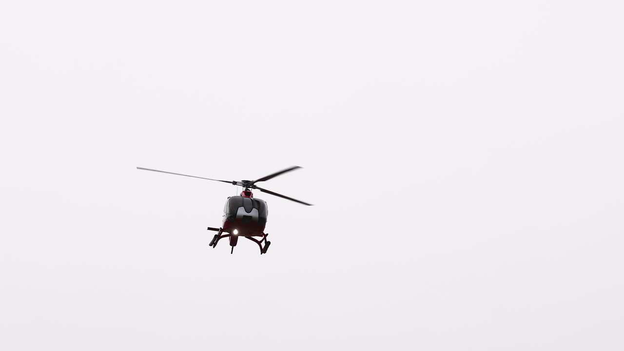 A helicopter flies over the scenic Great Ocean Road, captured in clear daylight with a focus on aerial movement and landscape