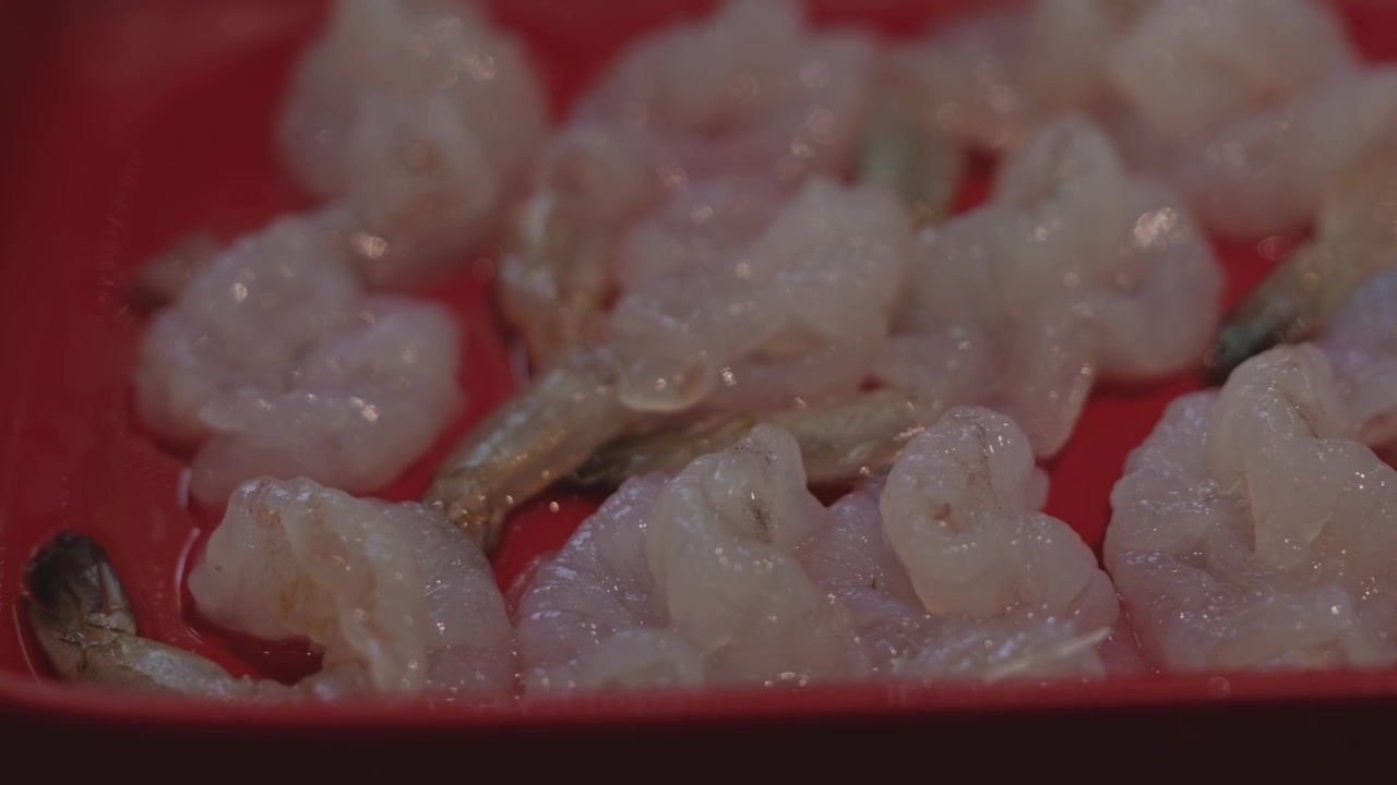 Primo piano di gamberi freschi sgusciati disposti ordinatamente su un piatto, preparati come ingrediente di mare per la cottura shabu shabu e hot pot