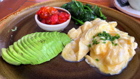 Traditional-healthy-Mediterranean-breakfast-in-Spain,-scrambled-eggs-with-avocado,-tomato-and-spinach,-4K-static-shot