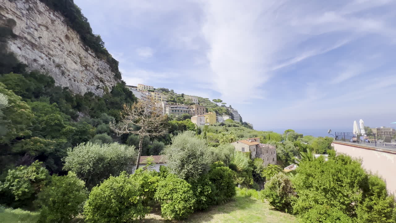 una exuberante ciudad en la ladera de la colina con vistas al mar, con edificios en terrazas y abundante vegetación bajo un cielo brillante - sorrento