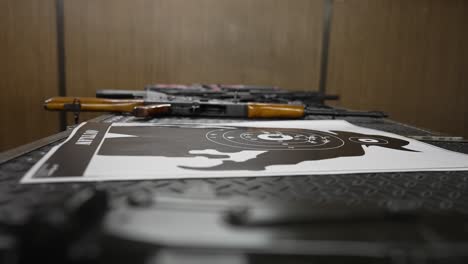 vista lateral de las armas y un objetivo utilizado con agujeros en él tendido en una mesa en un campo de tiro