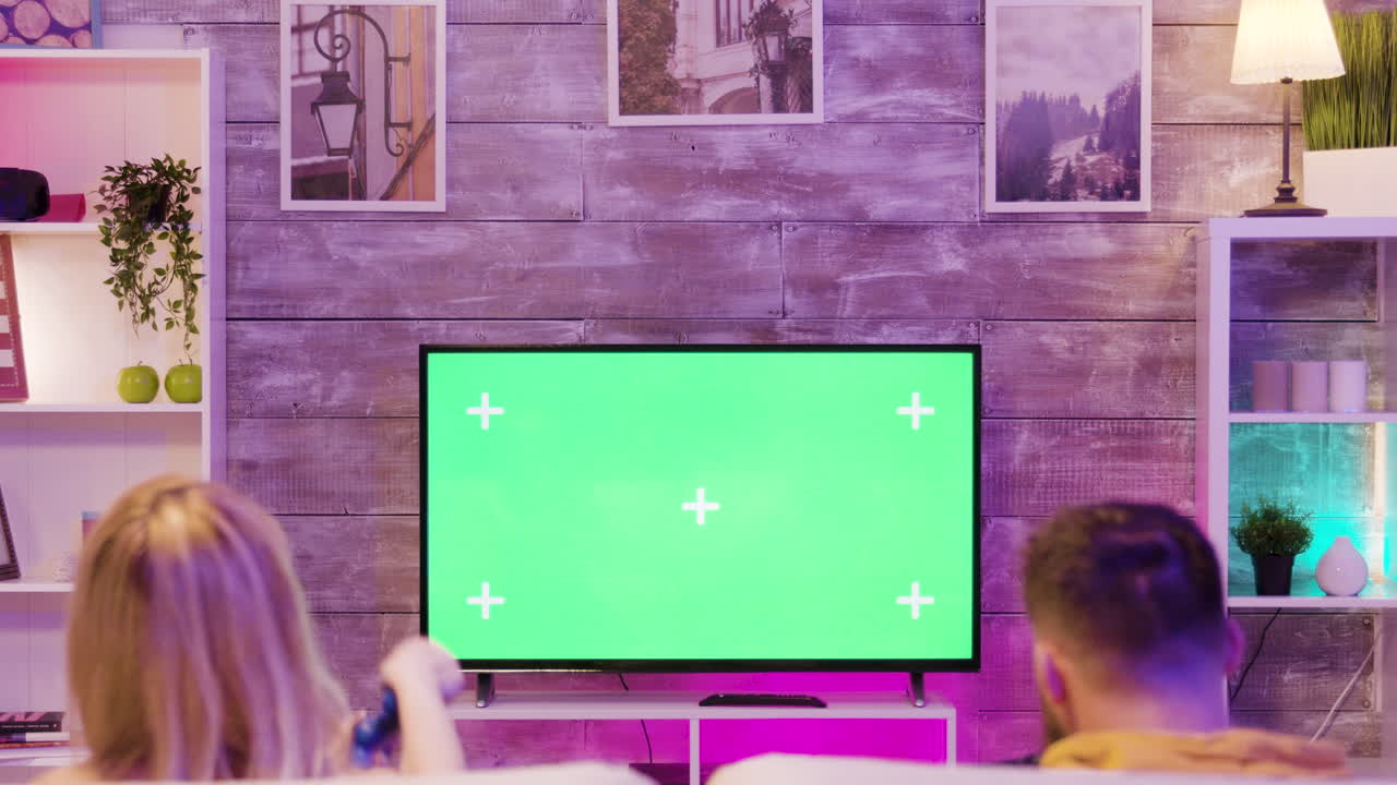 Couple playing video games on television with green screen in living room