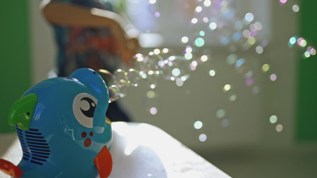 Boy's hand is switching on bubble device and playing happily at home. Bubble blower in the form of blue fish creating round bubbles into the room inside. Soap bubbles and small boy.