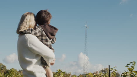 mom shows the baby a small family wind generator installed on their farm