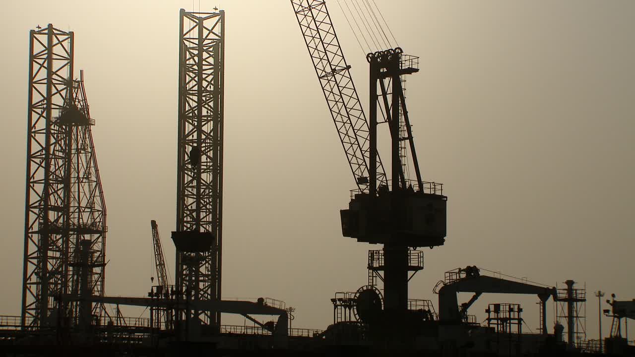 Moving shot from a boat of oil rigs close to port and dry dock awaiting repairs and re-deployment at sea in Bahrain in the Arabian Gulf