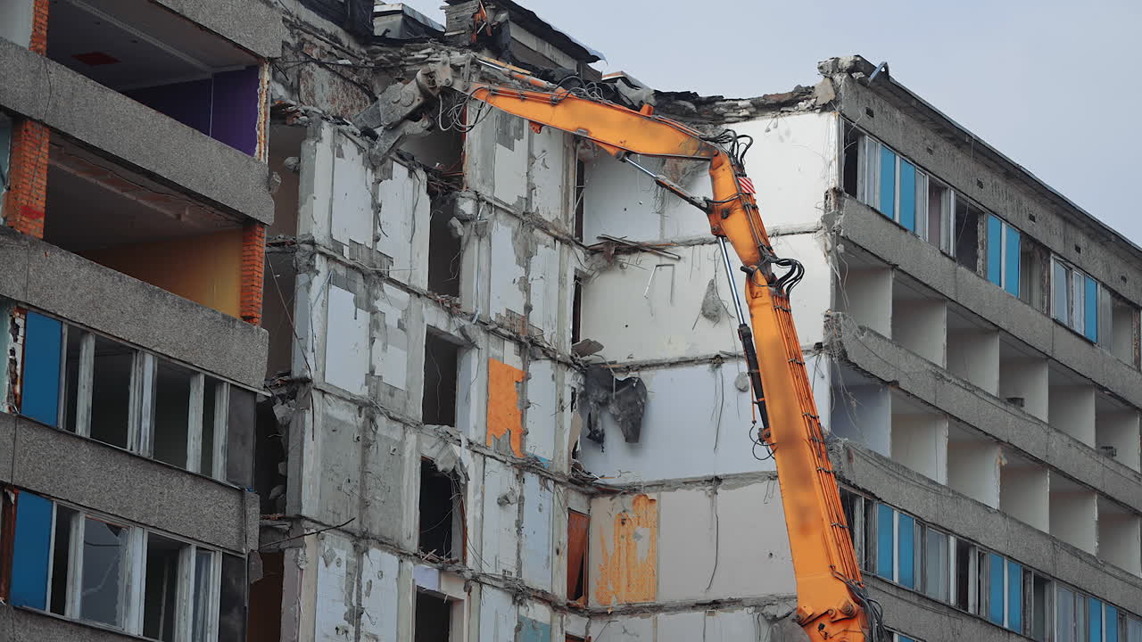Top floors destruction by the hydraulic claw of excavator. Demolition of old house building for new construction by excavator bucket. View from the below.