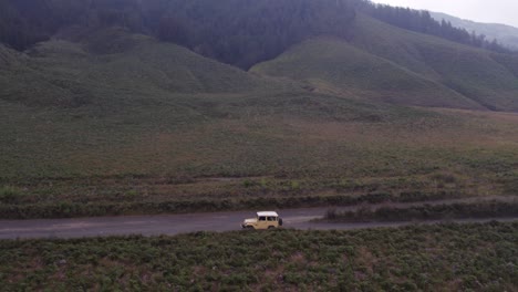 el avión no tripulado vuela alrededor del jeep amarillo que conduce por el camino de tierra en el monte bromo indonesia, aérea