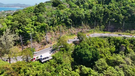 drone footage captures vehicles navigating a winding road through lush greenery in phuket, thailand, under bright daylight
