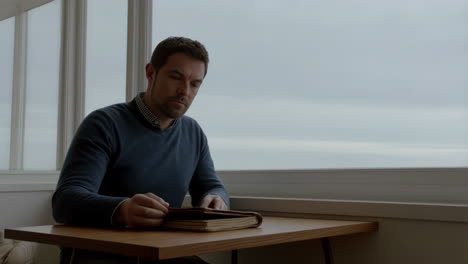 man at table with book looking out window