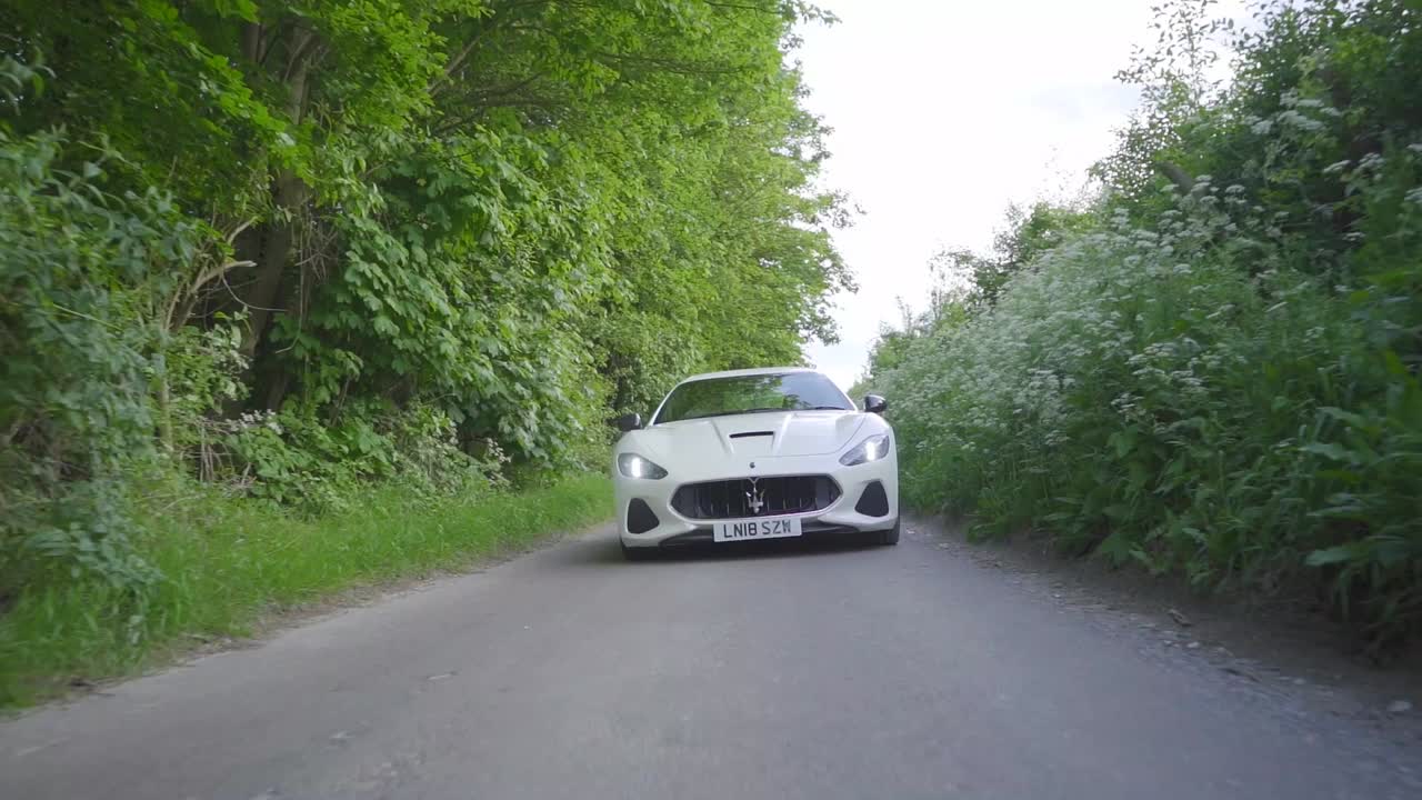 Maserati driving on road surrounded by nature