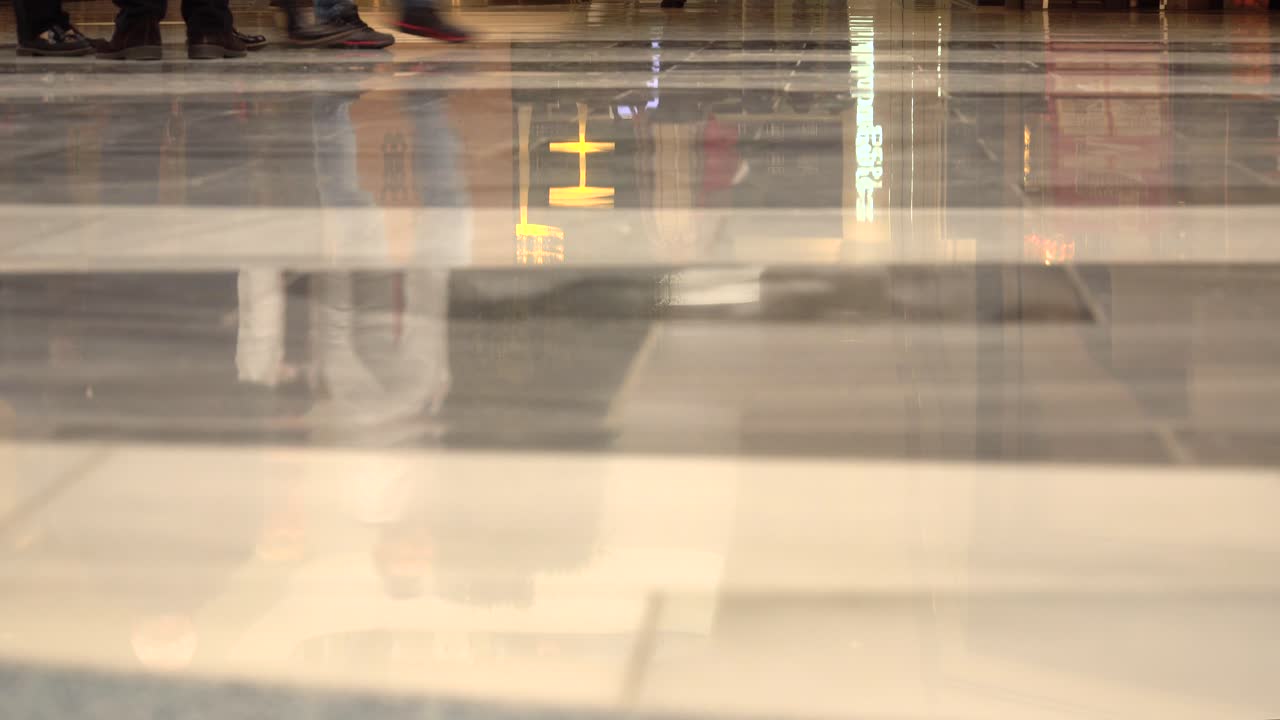 Reflections and feet only shot of people walking inside busy shopping mall