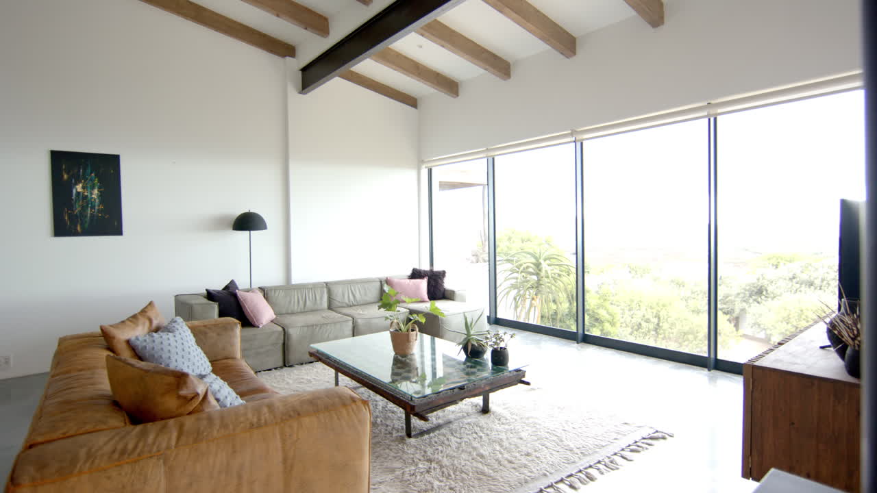 Modern living room with large windows, cozy sofas, and glass coffee table