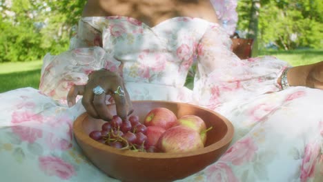 Mujer-Negra-Recogiendo-Uva-Y-Manzana-Del-Tazón-Comiendo-En-Un-Picnic-En-El-Parque,-De-Cerca