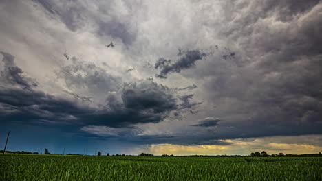 Stormy-clouds-move-above-green-fields-rural-road,-time-lapse-sunset-background