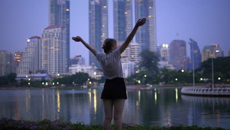 a woman raises her arms in celebration in front of a city across a lake