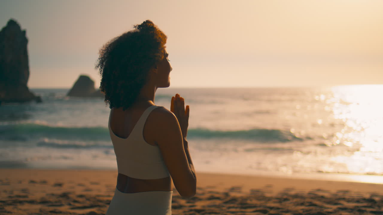 Back view woman meditating sitting with namaste hands in front sunrise close up.