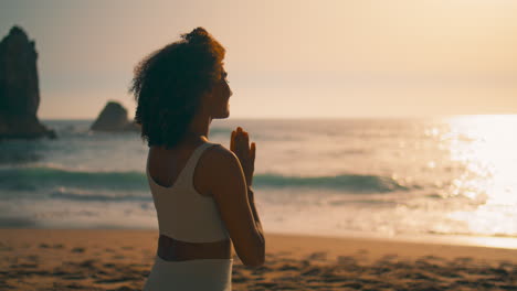 back view woman meditating sitting with namaste hands in front sunrise close up.