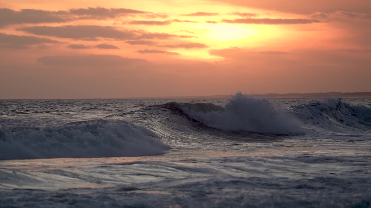 los tonos del atardecer proyectan un brillo cálido sobre las olas del océano, filmados en cámara lenta