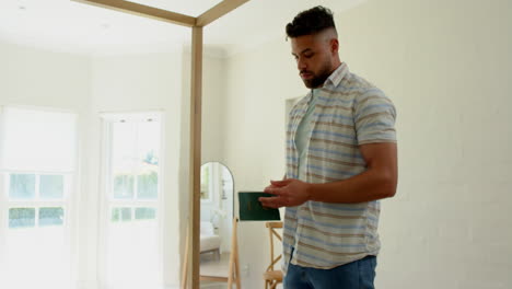 man using smartphone at home, standing near window, looking focused