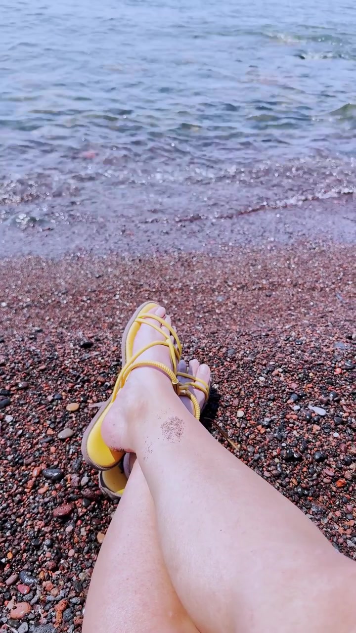 Gambe di donna che si rilassano sulla spiaggia rossa vulcanica a Santorini
