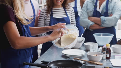 close up of female teacher adding mixture to pan in cookery class