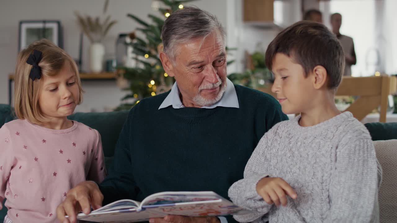 Uomo anziano caucasico che legge un libro ai bambini la Vigilia di Natale