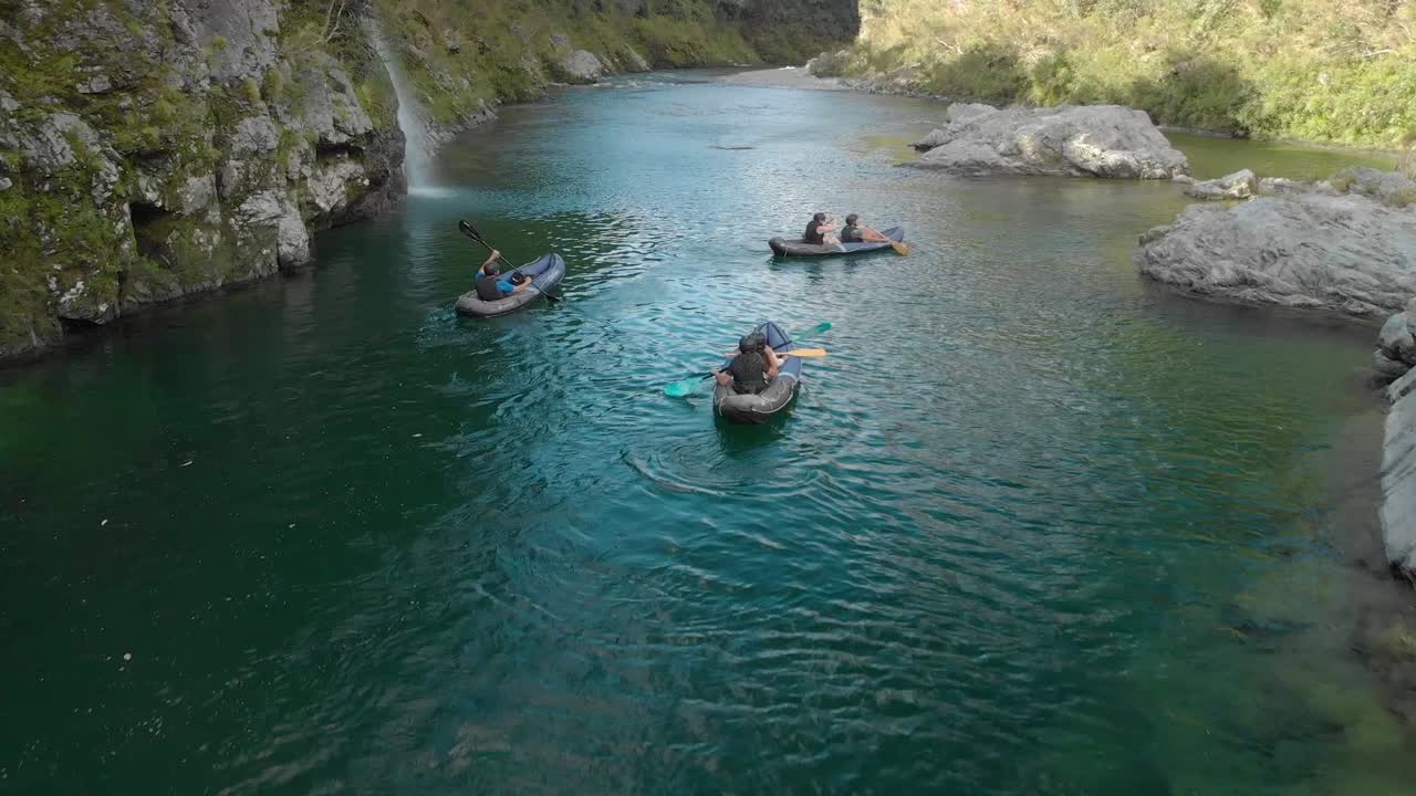 Rallentatore - Persone in gita in kayak remano attraverso un canyon sul fiume Pelorus, Nuova Zelanda, con foresta nativa e massi di roccia. Ripresa aerea con drone.