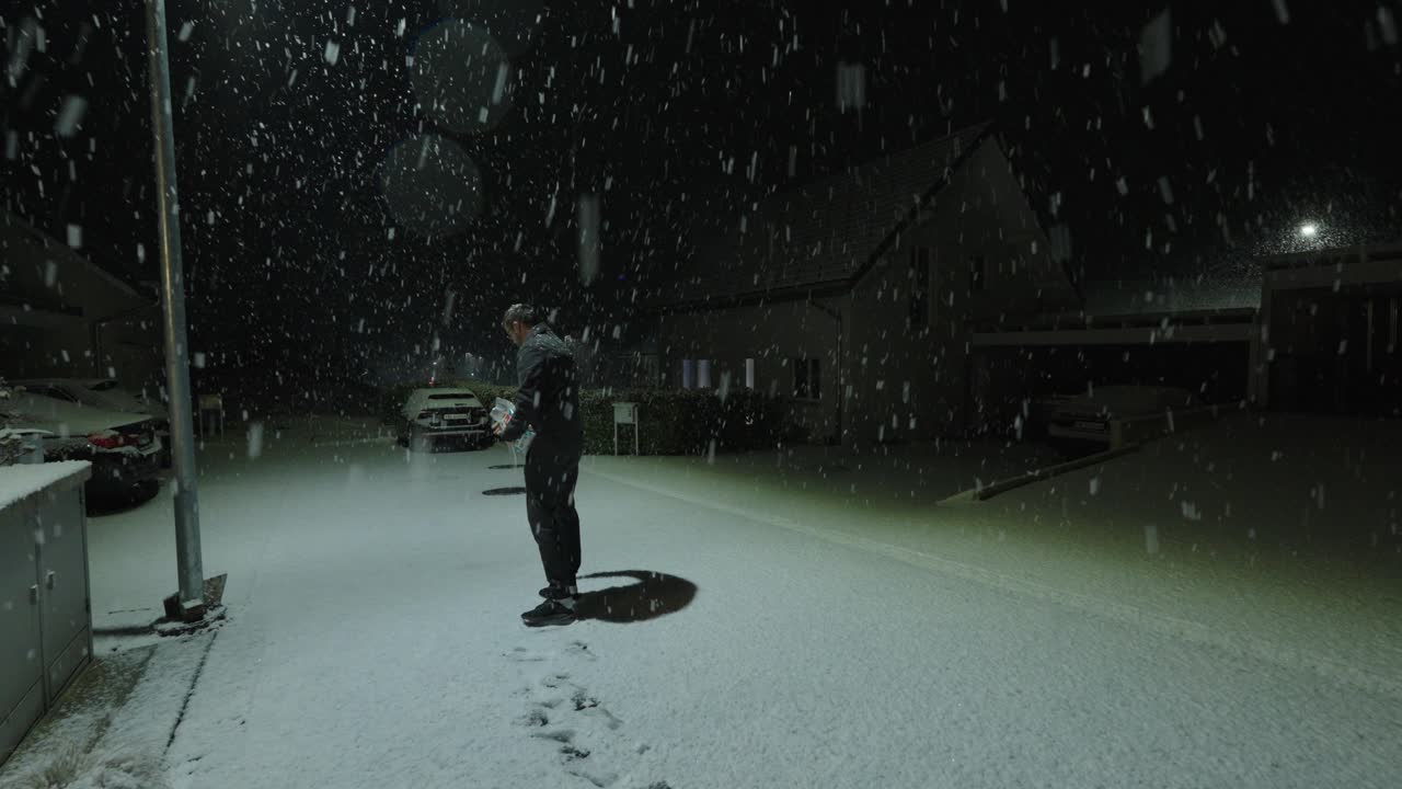 A man spreads salt on a snow-covered street at night while heavy snow is falling. Concept of winter safety, ice prevention, road maintenance, and personal responsibility in dangerous weather condition